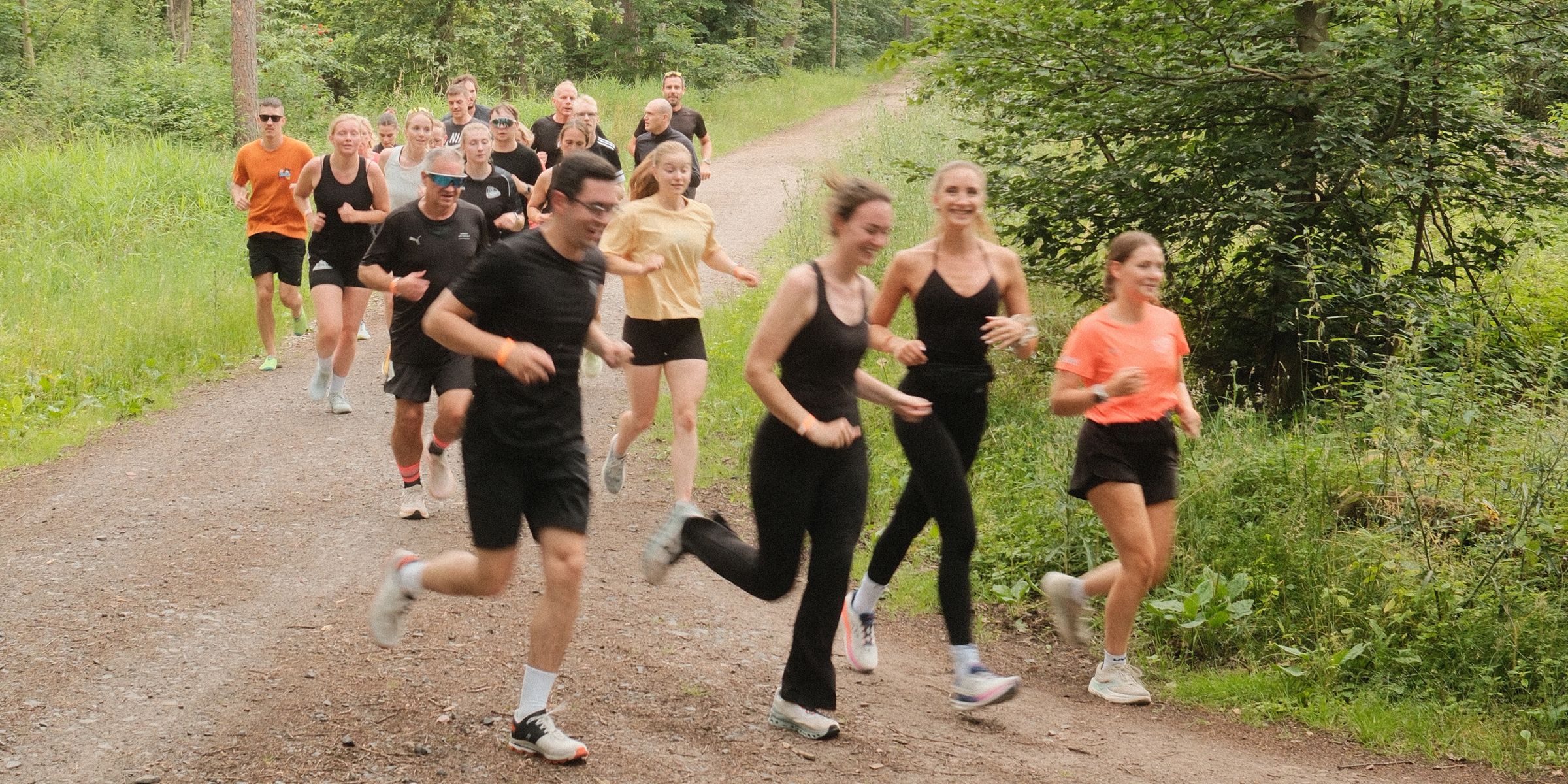 Laufgruppe von Tempo Zwei Lüneburg auf einem Waldweg, vorne lachen drei Läuferinnen